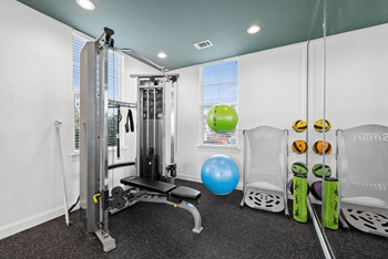 A gym with a weight machine, a bench, and exercise balls.